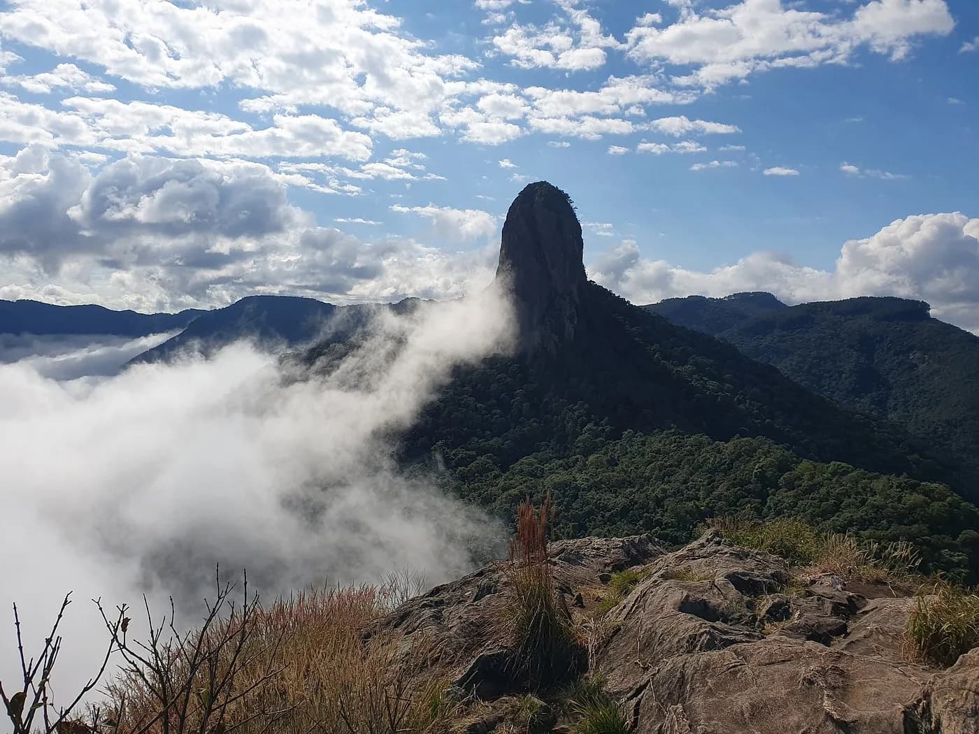 Monólito do complexo do Baú acima do mar de nuvens, visto de um cume vizinho de rocha exposta