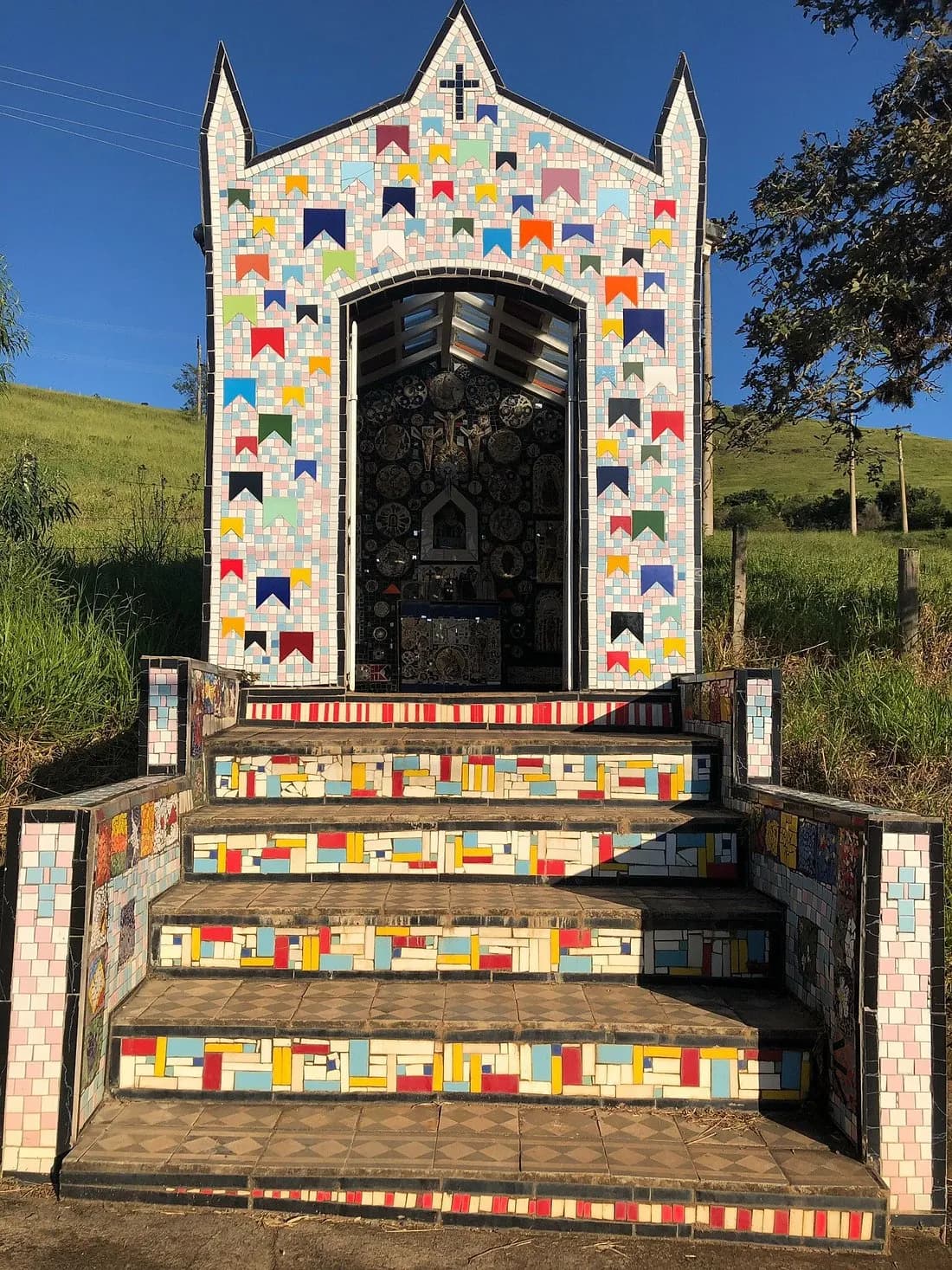 Altar de mosaico da capelinha, com nicho de santos e painéis de figuras nas paredes brancas