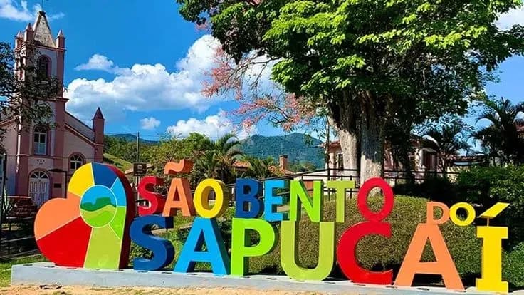 Letreiro colorido de São Bento do Sapucaí na Praça General Marcondes Salgado, com a igreja de torre única ao fundo