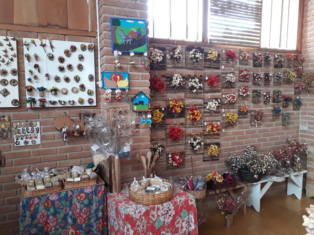 Interior da loja com arranjos de flores secas, ímãs artesanais e cestas sobre mesas de toalha floral