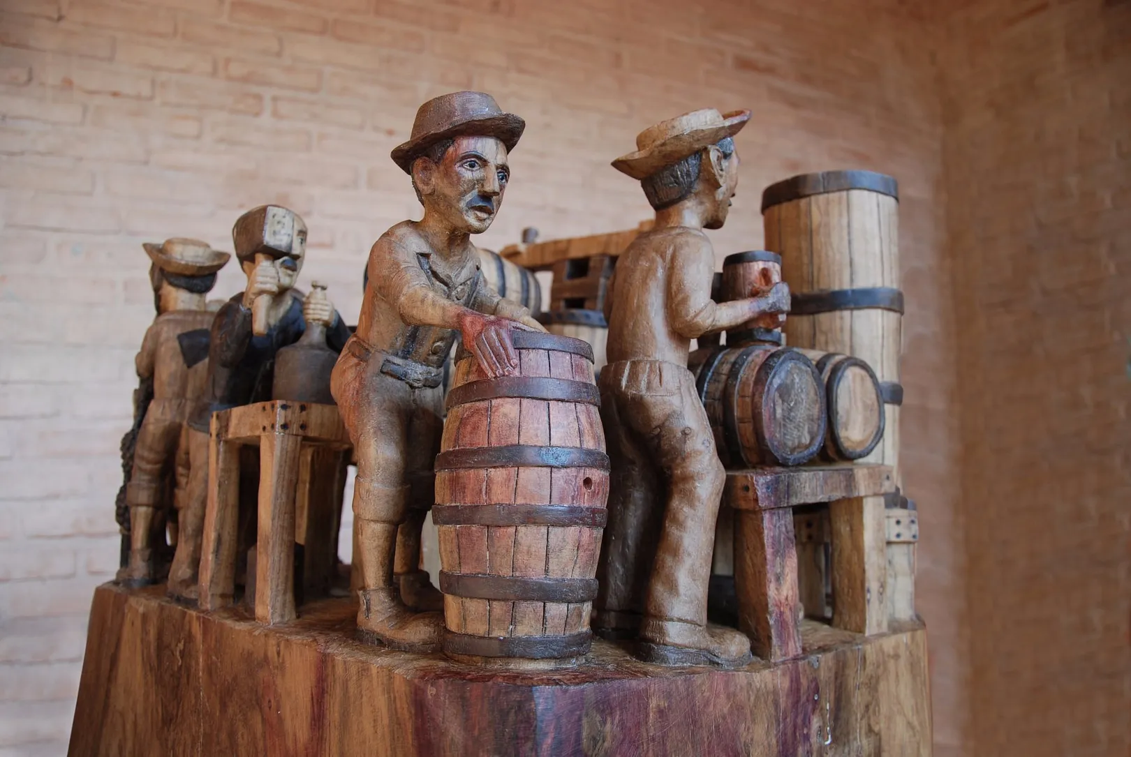 Escultura talhada num tronco único: figuras de chapéu em volta de um barril, dentro de uma venda antiga