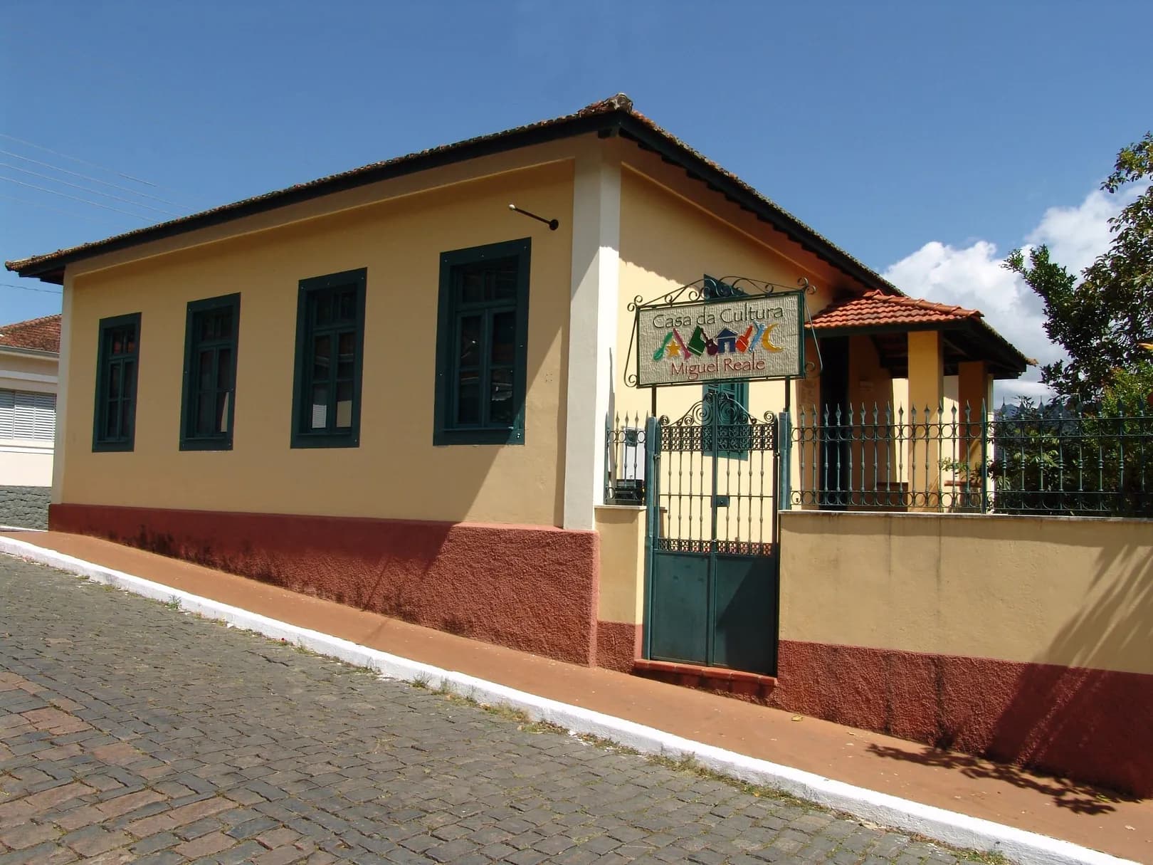 Fachada amarela da Casa da Cultura Professor Miguel Reale, com janelas verdes, no centro de São Bento do Sapucaí